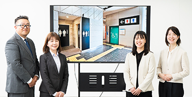 座談会に参加したメンバーが、東京ビッグサイト駅のトイレ付近を映し出したモニターを囲んで微笑んでいる