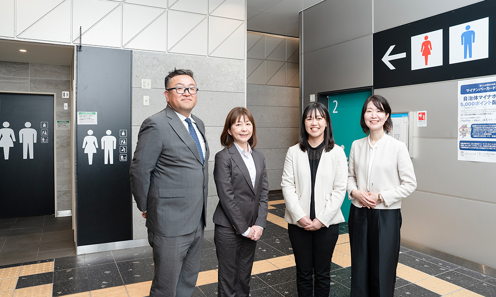 ゆりかもめ　東京ビッグサイト駅の男女共用トイレの前で、座談会のメンバー4人が並んで立ち微笑んでいる