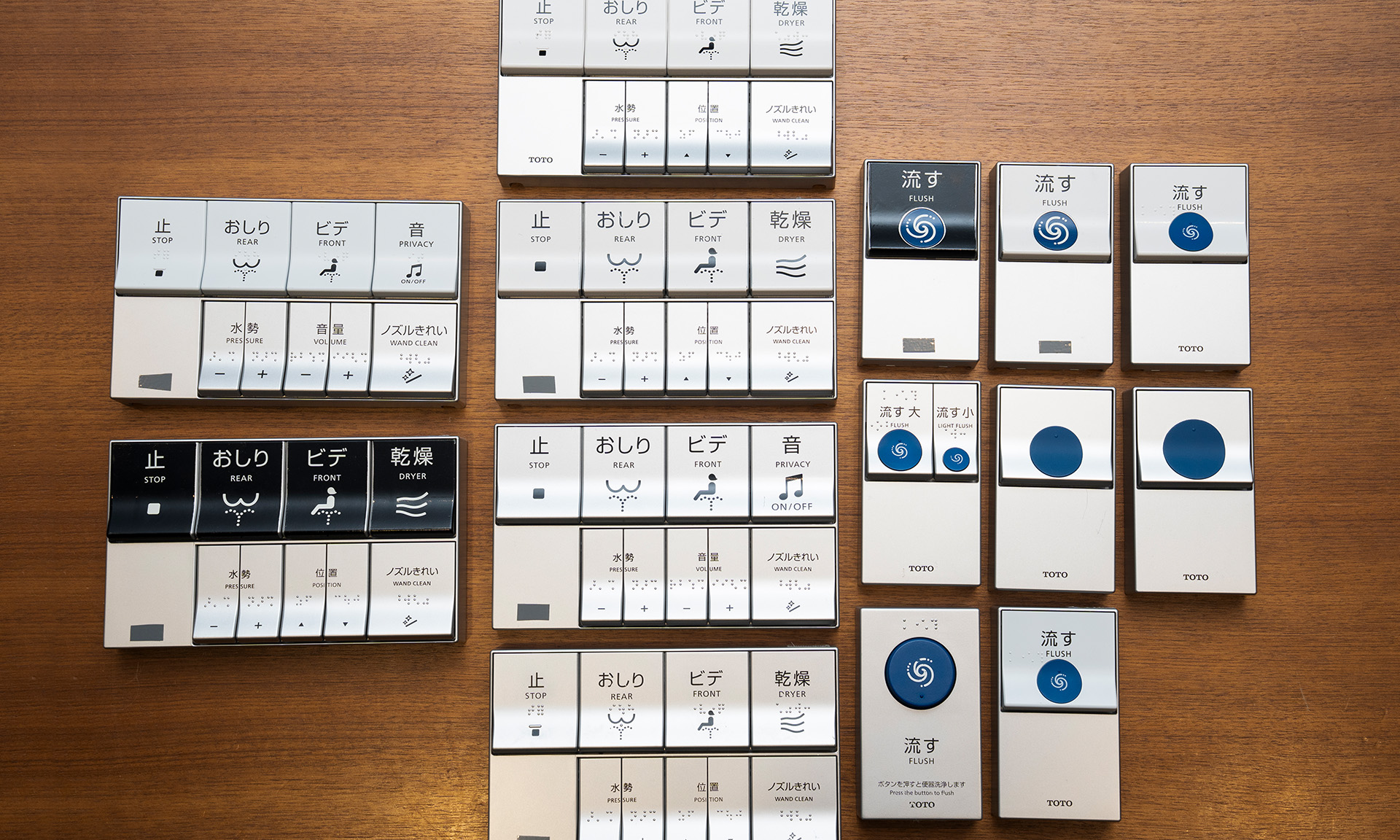 6タイプほどの試作品が並んでいる。ウォシュレットリモコン上段     のボタンや便器洗浄ボタンを黒にして文字を白くしたものもある