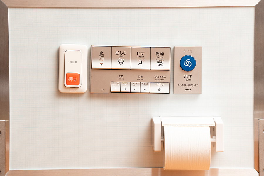 公共トイレ操作系JISに従ってボードに配置した呼出ボタン、ウォシュレットリモコン、便器洗浄ボタン、トイレットペーパーホルダー