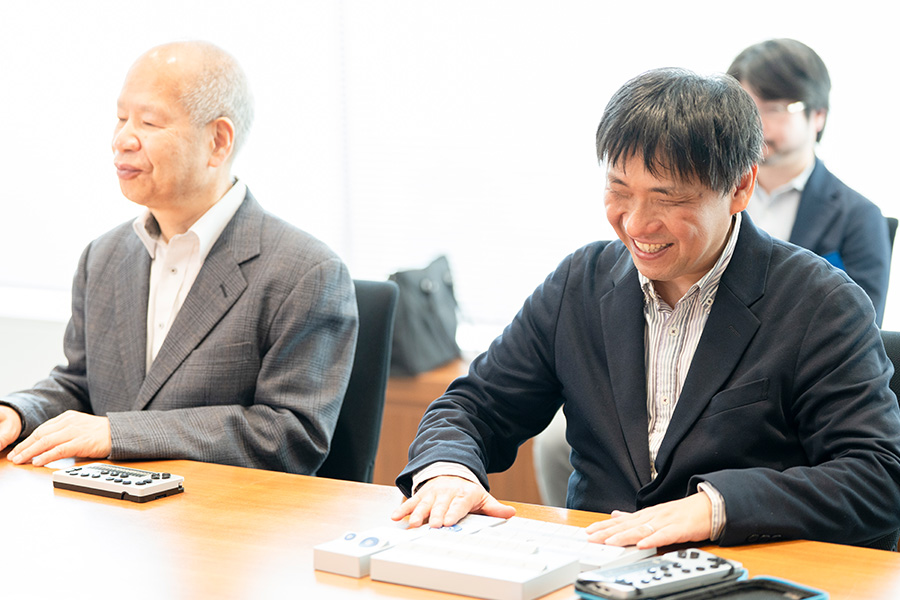 椅子に座り、笑顔でリモコンを触る大河内さん